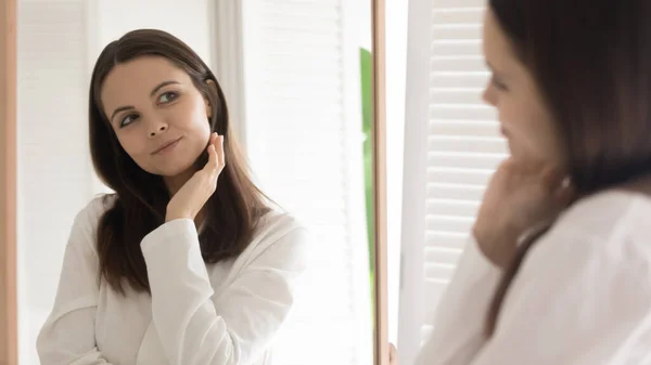 Tevreden mooie jonge vrouw op zoek naar spiegel in badkamer — Stockfoto