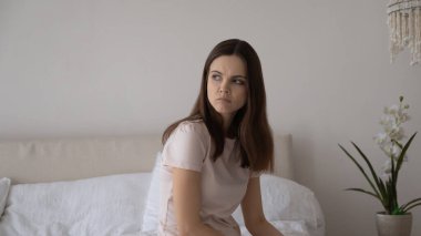 Mutsuz, depresif, düşünceli, genç bir kadın evde yatağında oturuyor.