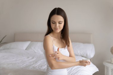 Genç ve güzel bir kadın koluna nemlendirici krem sürüyor.