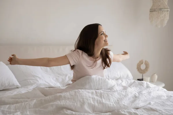 Lächelnde junge Frau sitzt mit ausgestreckten Händen im gemütlichen Bett — Stockfoto