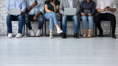 Elinde elektronik cihazlarla sırada oturan altı etnik çeşitliliğe sahip genç