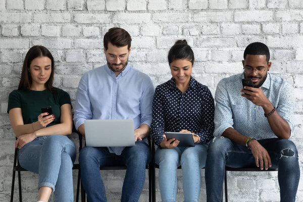 Мультирасовая молодежь сидит в помещении с различными электронными мобильными устройствами
