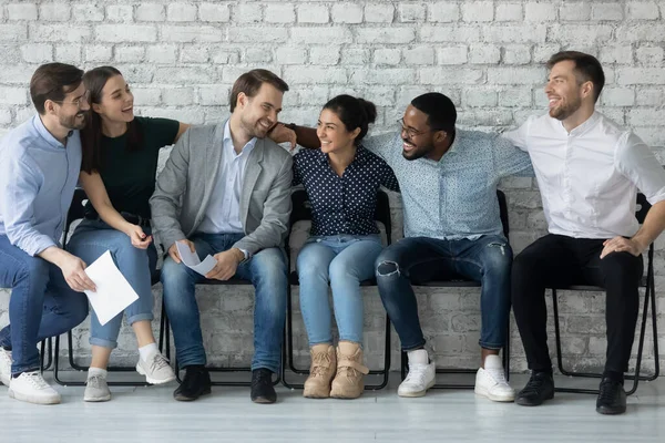 Los empleados multiétnicos se sientan en sillas en el pasillo de la oficina disfrutan de la comunicación — Foto de Stock