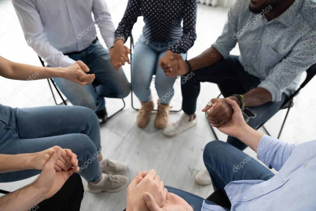 People sitting in circle holding hands involved at group therapy