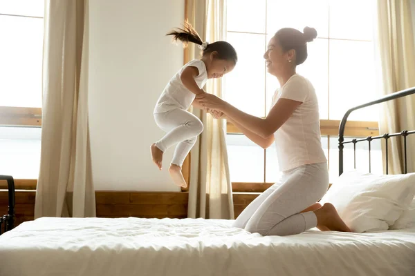 Asian small baby jumping on bed, holding hands of mum.
