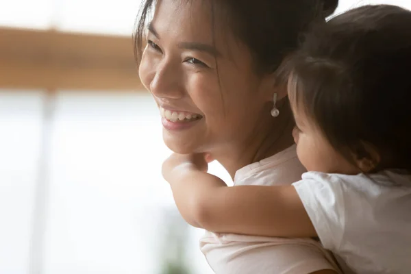 Gelukkig jong aziatische etniciteit vrouw dragen op terug schattig dochter. — Stockfoto