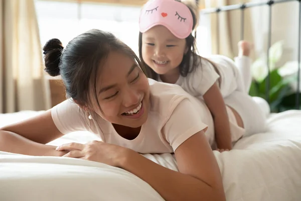 Gyönyörű vietnámi nő fekszik az ágyon a lányával a hátán. — Stock Fotó