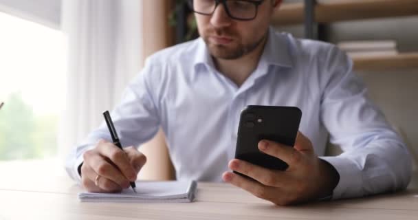 Zakenman met behulp van smartphone schrijven nuttige informatie werken binnen — Stockvideo