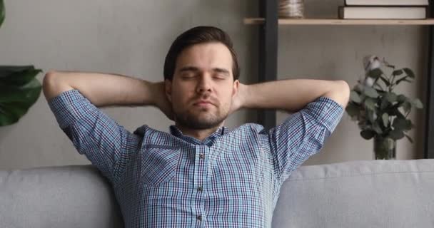 Homem calmo coloca as mãos atrás da cabeça descansando magra no sofá — Vídeo de Stock