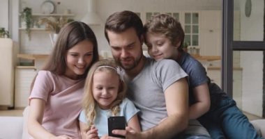 Çocuklu mutlu ebeveynler evde akıllı telefon kullanarak eğleniyorlar.