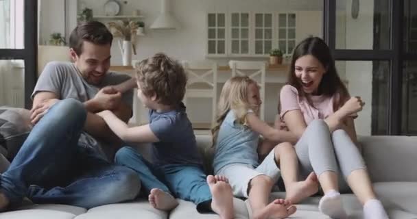 Счастливые родители с маленькими щекотаниями смеются, играя на диване вместе — стоковое видео