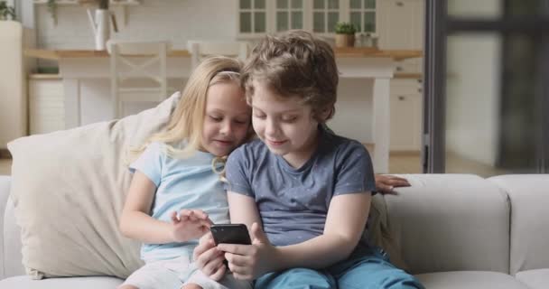 Двое веселых детей-братьев и сестер, играющих на смартфоне дома в игры — стоковое видео