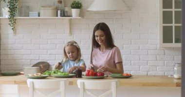 Tatlı kız annesine mutfakta salata keserken yardım ediyor.