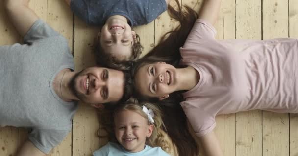 Щасливі батьки і діти лежать на теплій дерев'яній підлозі, портрет — стокове відео