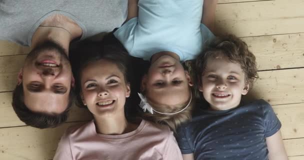 Famiglia felice con bambini che guardano la macchina fotografica sdraiati sul pavimento — Video Stock