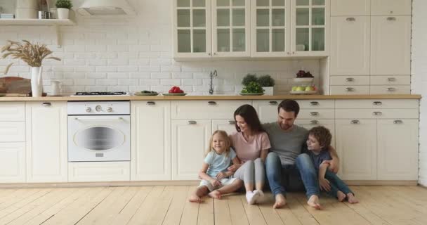 Счастливые родители и дети смеются сидят на полу на кухне — стоковое видео