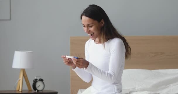 Mujer joven emocionada sentarse en la cama sosteniendo positivo prueba de embarazo — Vídeo de stock