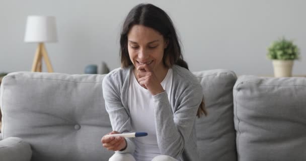 Giovane donna incinta felicissima con test di gravidanza seduta sul divano — Video Stock