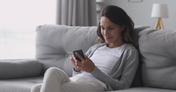 Šťastná mladá žena pomocí telefonu sedět na gauči doma — Stock video