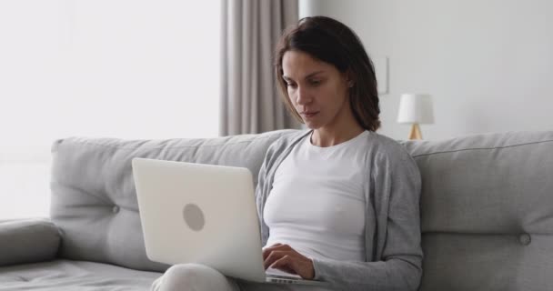 Орієнтована молода жінка фрілансер студент, використовуючи ноутбук, сидячи на дивані — стокове відео