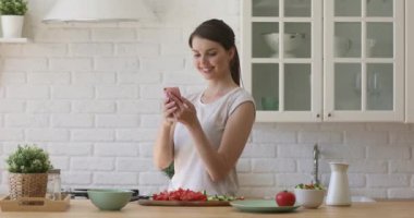 Gülümseyen genç kadın mobil uygulamalar kullanarak sağlıklı sebze salatası hazırlıyor.