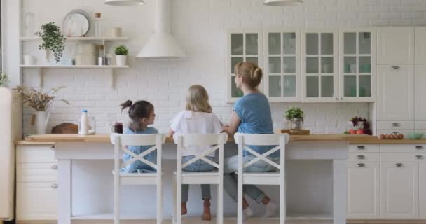 Moeder en dochters zitten op stoelen in de keuken, achteraanzicht — Stockvideo