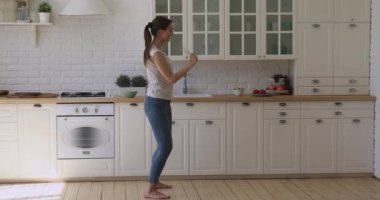 Elinde mikrofonla dans eden neşeli kız mutfakta şarkı söylüyor.
