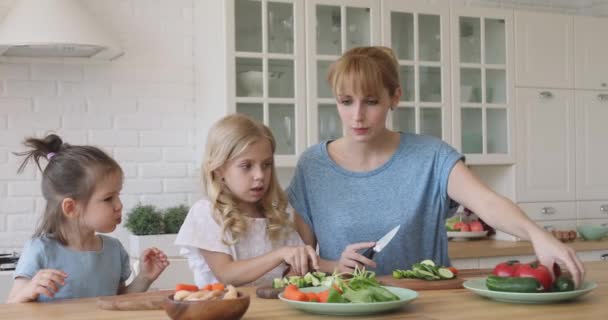 Divertidos niños hermanos ayudando a mamá a cortar ensalada de verduras frescas juntos — Vídeo de stock