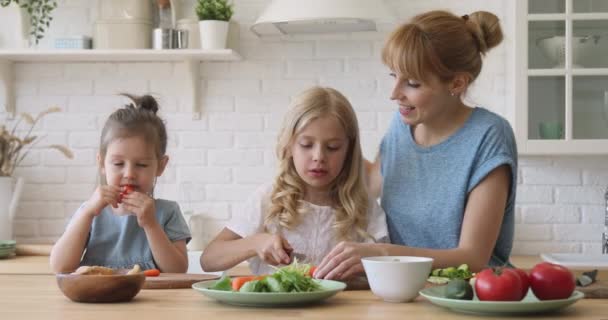 Jovem mãe ensinando crianças filhas cortando salada vegetal na cozinha — Vídeo de Stock