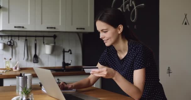 Женщина, стоящая на кухне с карточкой с компьютером делает покупки — стоковое видео