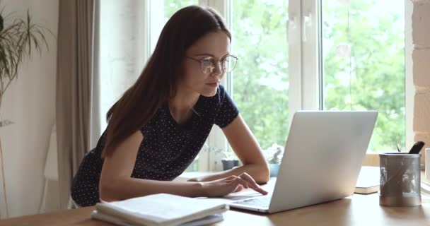 Студентка носит очки, ищет информацию, печатающую на компьютере — стоковое видео