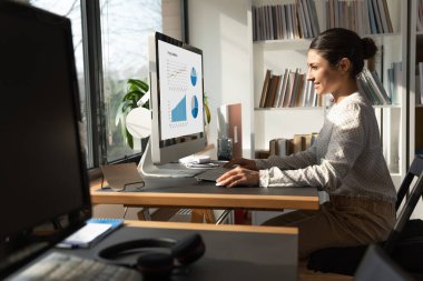 Ofiste bilgisayar üzerinde çalışan mutlu Hintli kadın çalışan.