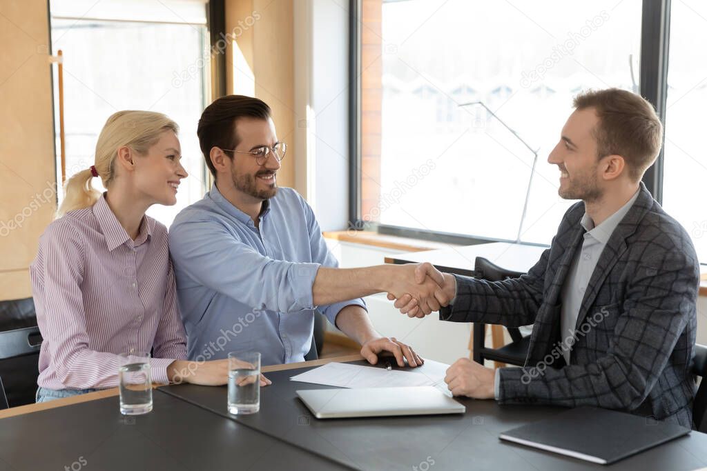 Excited Caucasian couple shake hand of male realtor