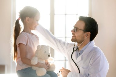 İlgilenen erkek doktor hastanede küçük kız hastayı okşuyor.