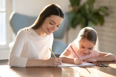 Gülümseyen kadın sevimli küçük kızıyla renkli kalemler çiziyor.