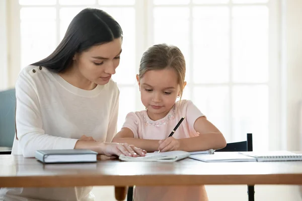 Cuidar a la madre ayudando a la pequeña hija con la tarea, estudiando en casa — Foto de Stock