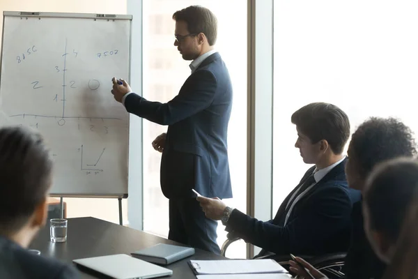 Zaměřený mladý obchodní trenér vysvětlující ručně kreslené grafy na tabuli. — Stock fotografie