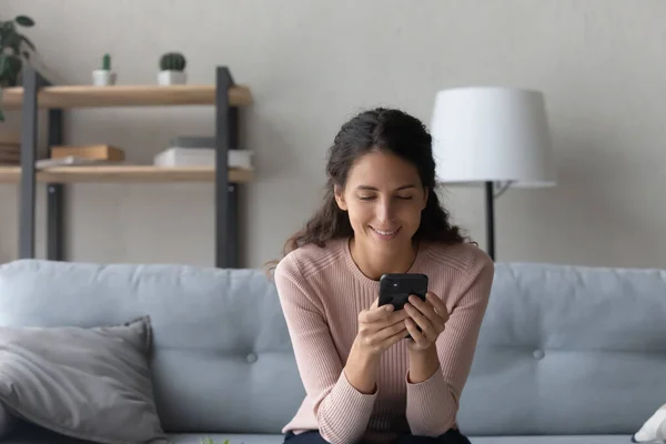 Happy millennial woman browsing internet on cellphone at home