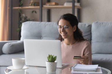 Gülümseyen genç kadın evde online alışveriş yaparken eğleniyor.