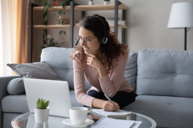 Kulaklık takmış genç bir kadın dizüstü bilgisayarda webinar izliyor.
