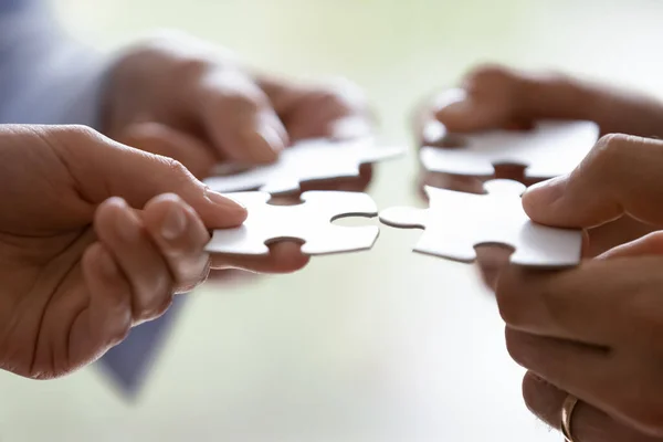 Hands of four businesspeople holding pieces of white puzzles close up — Stock Photo, Image