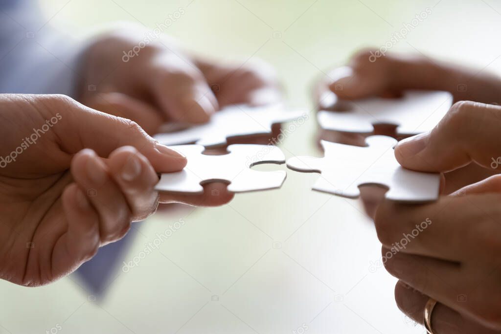 Hands of four businesspeople holding pieces of white puzzles close up