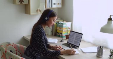 Öğrenci kız kulaklık takıyor. Sınavlara hazırlanıyor. Kompozisyonu not alıyor.