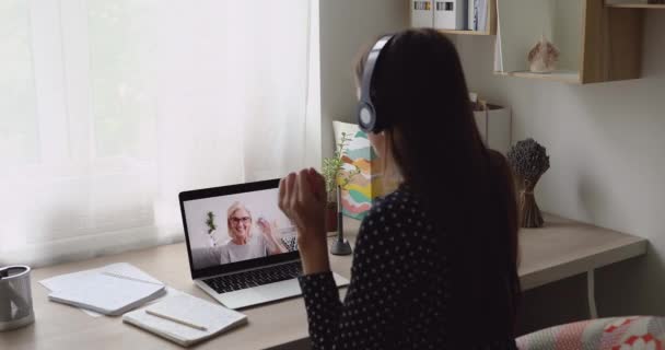 Junge Frau trägt Kopfhörer im Gespräch mit betagter Frau per Videotelefon — Stockvideo