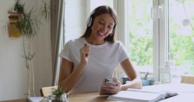 Kulaklık takan bir kız elinde akıllı telefonuyla arkadaşlarıyla görüntülü konuşma yapıyor.