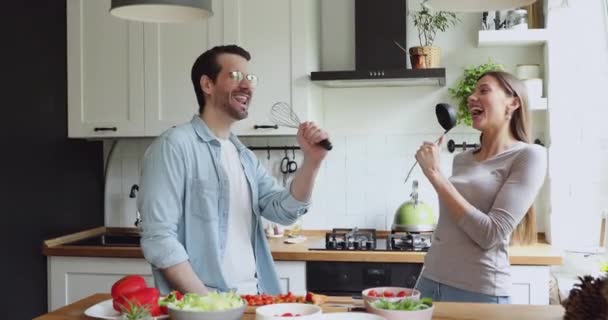 Paar benutzt Küchenutensilien wie Mikrofone, die in der Küche ein Lied singen — Stockvideo