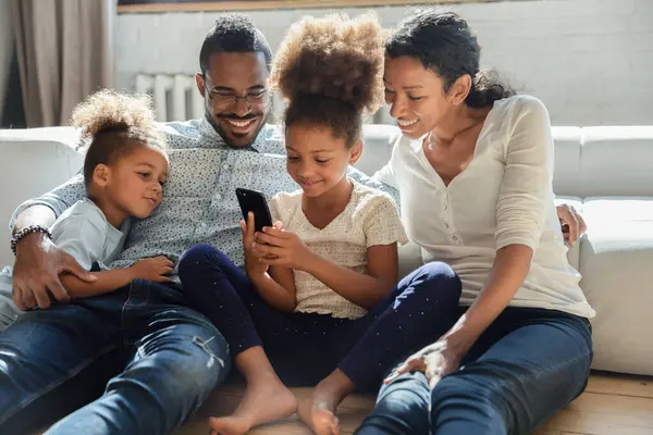 Amar a jovem família biracial com crianças usando smartphone em casa — Fotografia de Stock