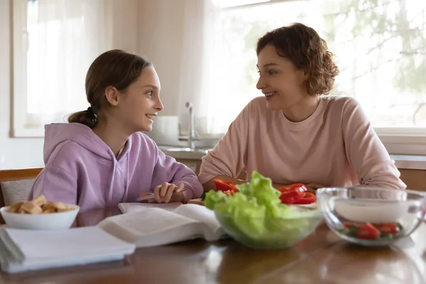 Счастливая мать и дочь-подросток болтают, сидят на кухне — стоковое фото
