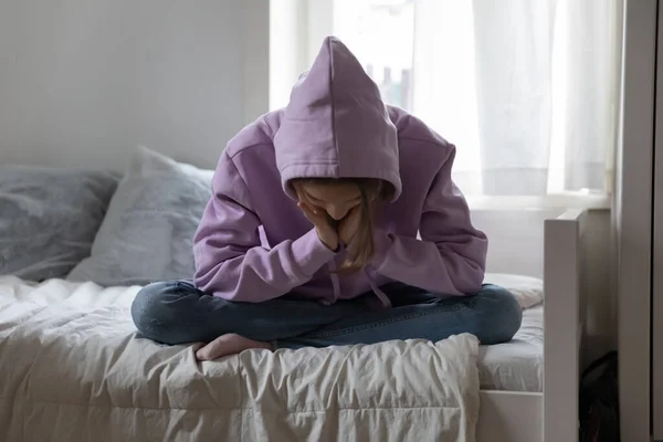 忧心忡忡的少女穿着运动衫一个人坐在床上 — 图库照片