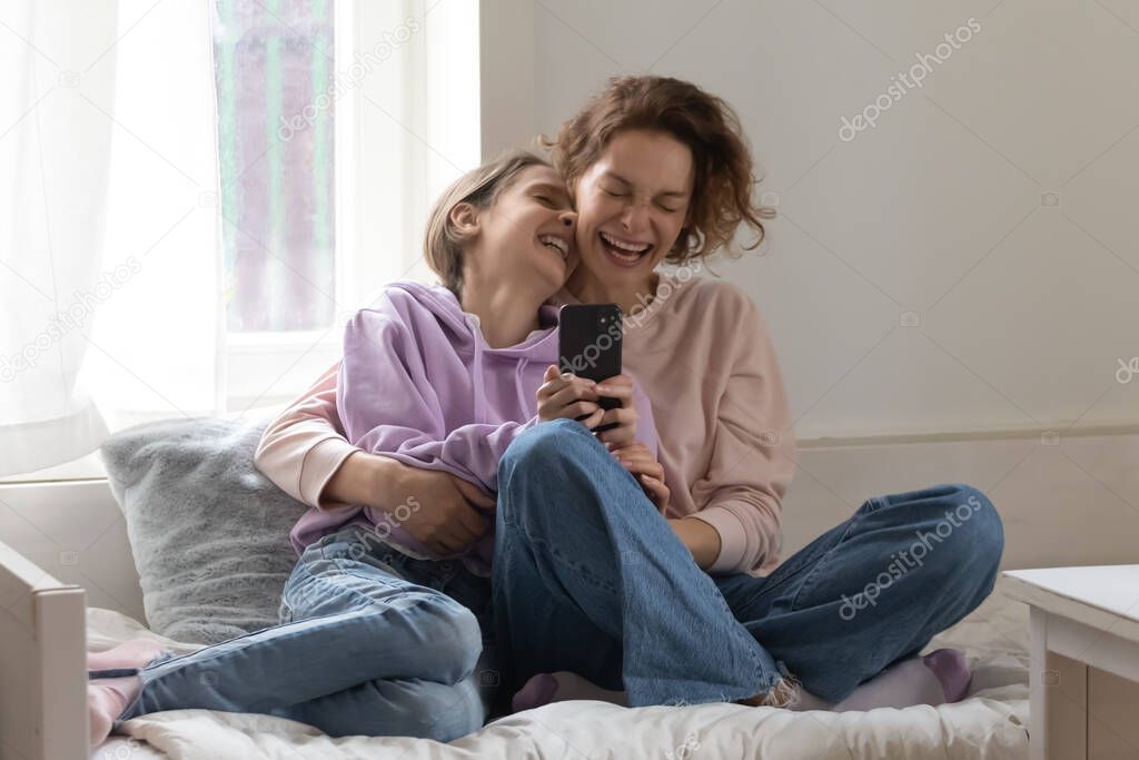 Overjoyed mother and teenage daughter having fun with smartphone
